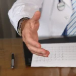 Médico con bata tendiendo la mano en su consulta